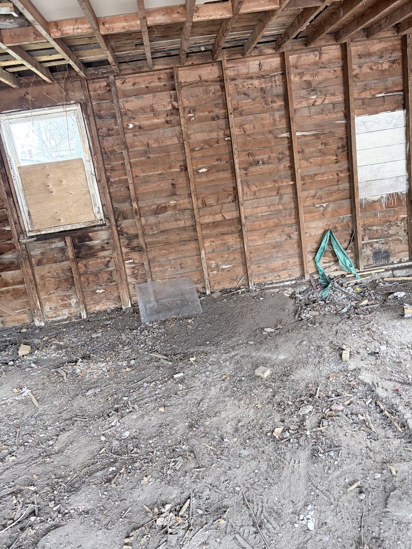 The same shed emptied down to the bare dirt floor and open board walls