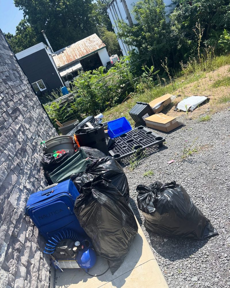 A narrow Kingston side yard piled with garbage bags, luggage and an air compressor waiting for pickup