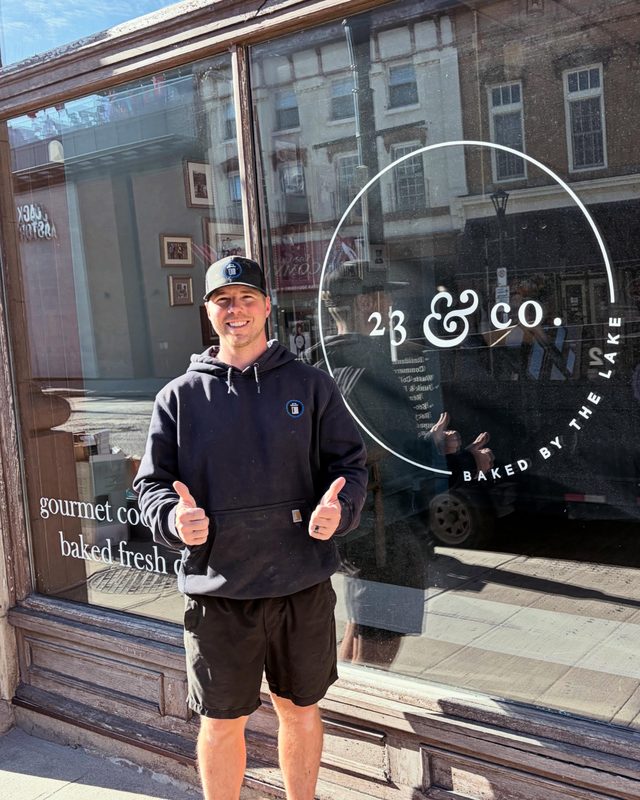 Brock outside 2B & Co. bakery on Princess Street, giving a thumbs up in front of the storefront window