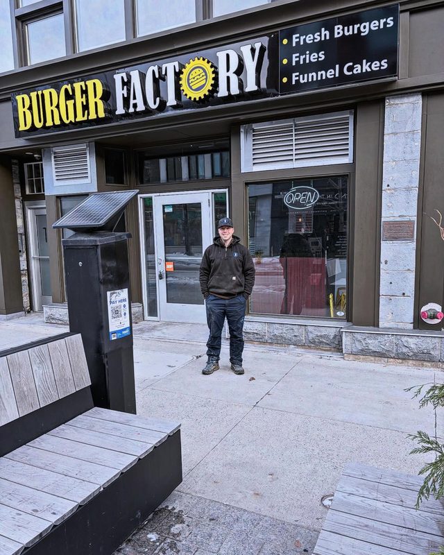 Brock outside Burger Factory, standing on the sidewalk beneath the storefront sign
