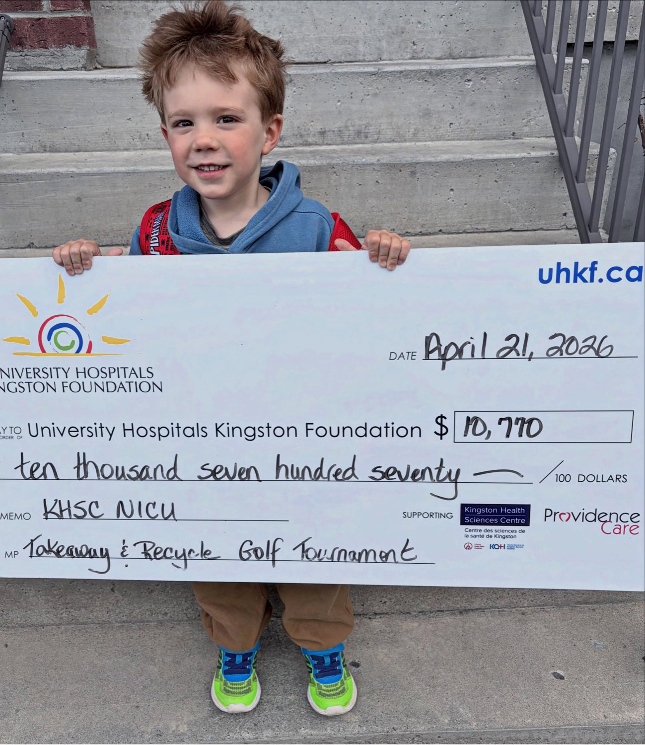 A child holding the oversized cheque for $10,770 made out to the University Hospitals Kingston Foundation, memo KHSC NICU, from the TakeAway and Recycle Golf Tournament