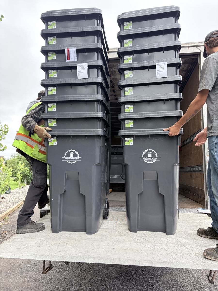 Two crew members loading stacks of new branded TakeAway & Recycle wheelie bins into the back of a truck