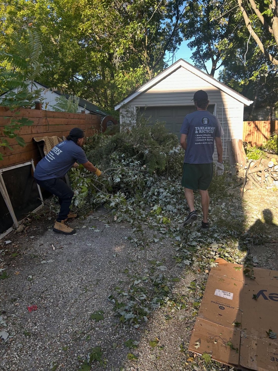 Two crew members in branded TakeAway & Recycle shirts clearing fallen branches from a Kingston driveway