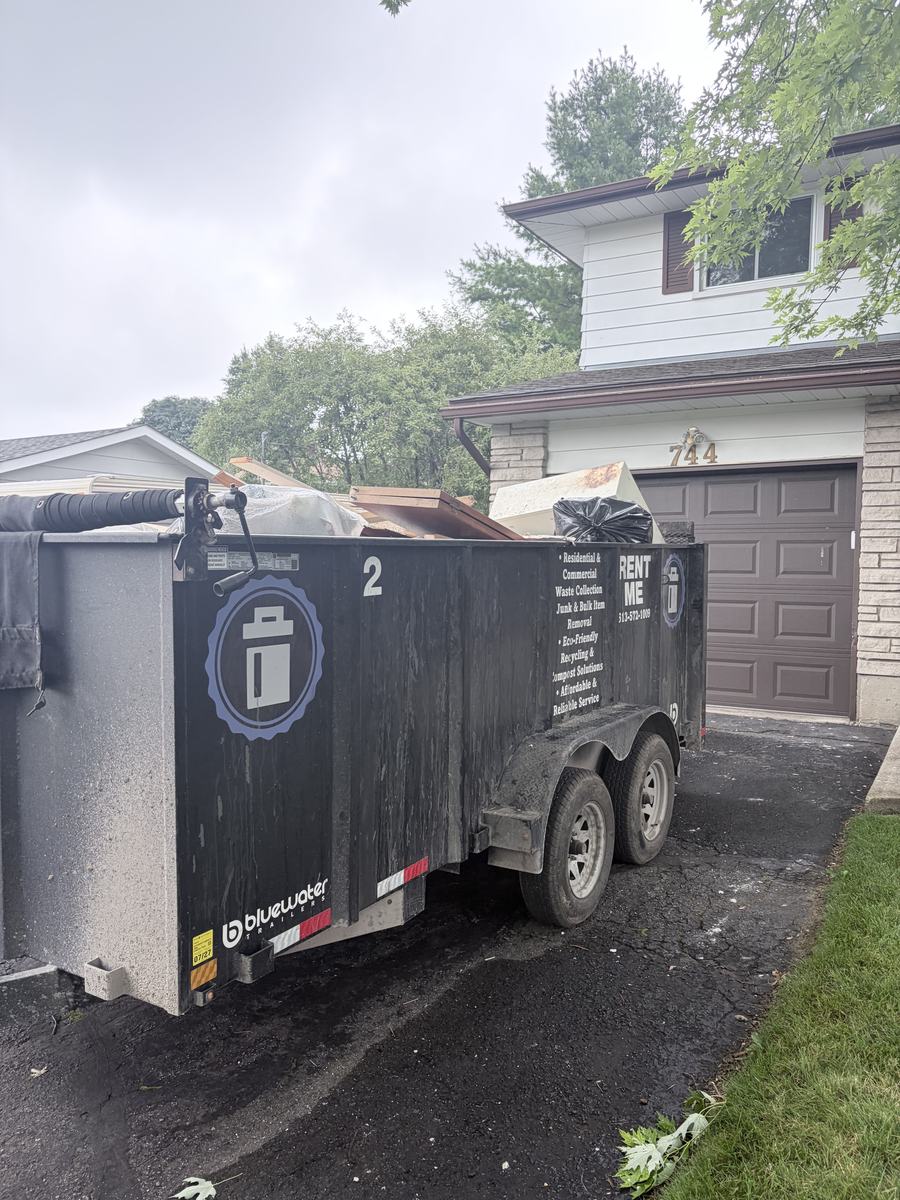 A 14-yard TakeAway & Recycle bin parked in a suburban driveway, filled with renovation lumber and bagged debris