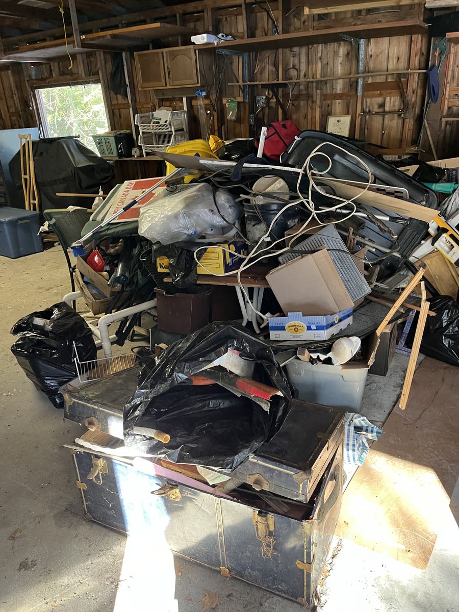 A garage packed shoulder-high with old furniture, luggage, tools and bagged household junk before a cleanout