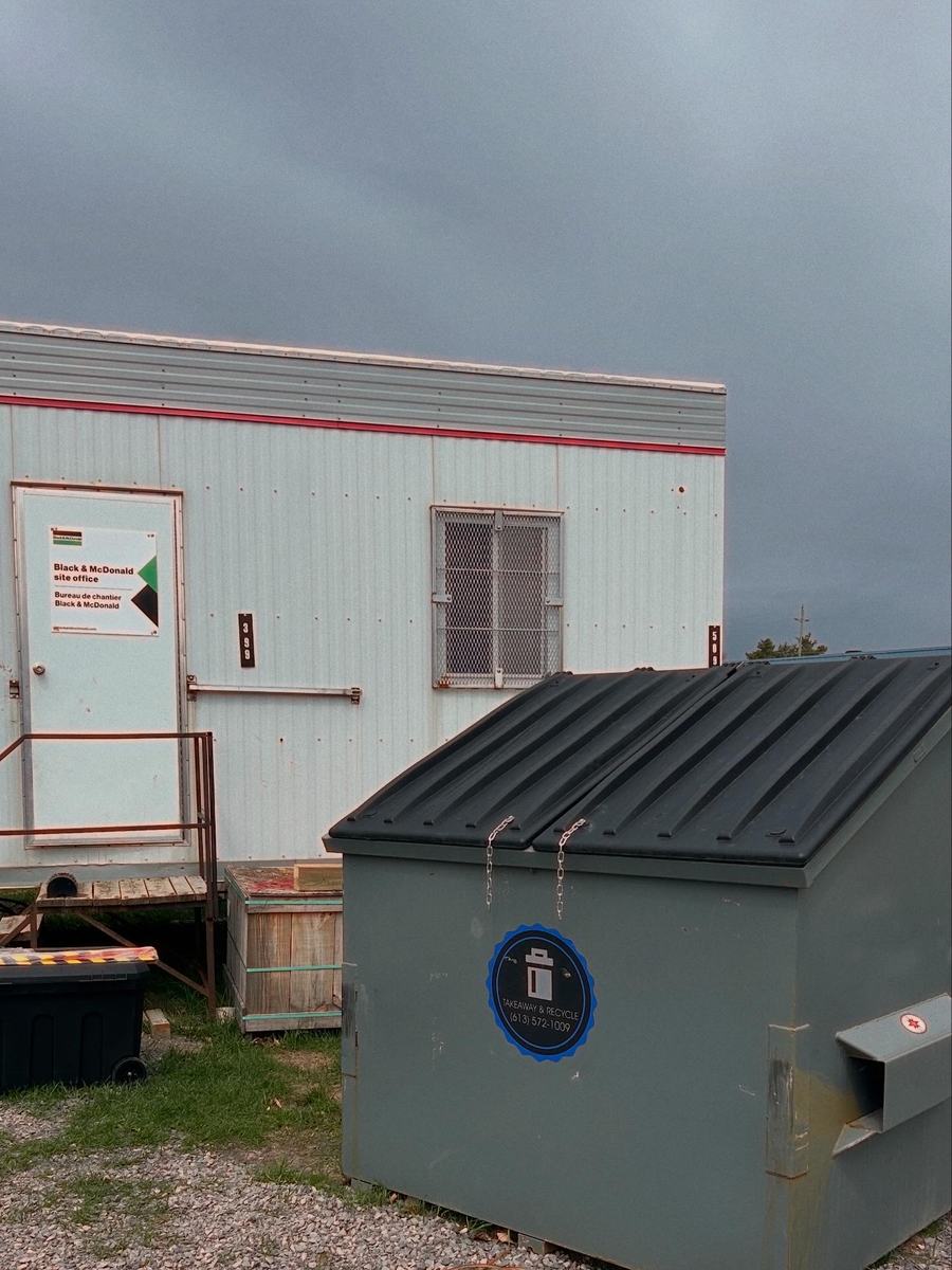 A TakeAway & Recycle front-load bin beside a construction site office trailer under a dark sky