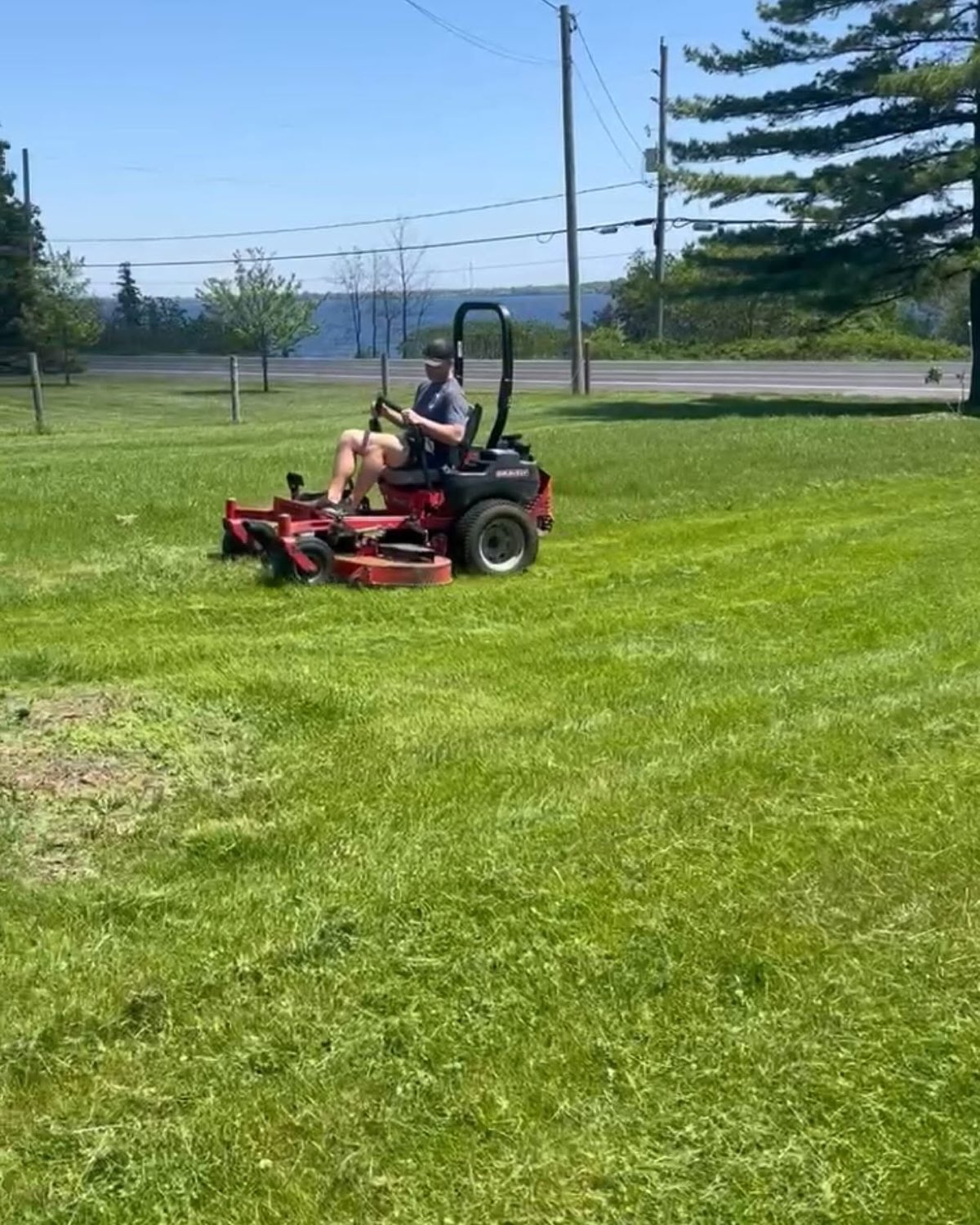 A crew member on a zero-turn mower cutting a large waterfront lawn
