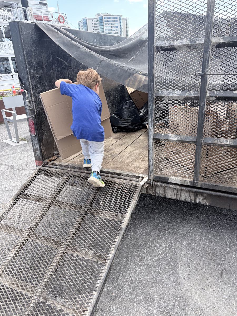 A small child in a blue shirt carrying a flattened box up the ramp into the trailer on the Kingston waterfront