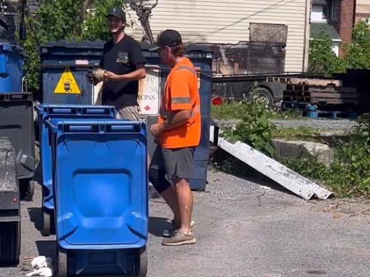Two TakeAway & Recycle crew members wheeling blue curbside recycling bins down a Kingston back lane